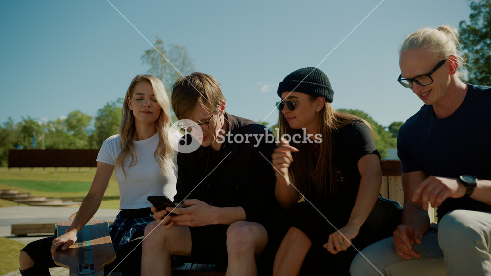 Stylish Cool Teenagers Chilling on the Benches in the Park, Using Smartphone. Two Girls and Two Boys Talking and Having Fun on Social Media. Hip Park In Gentrified Part of City