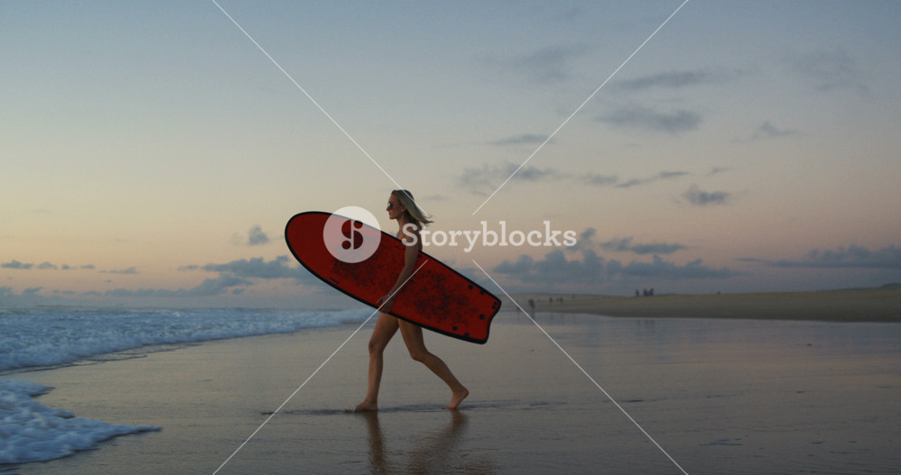 Side View Footage of the Beautiful Young Woman in the Swimsuit Walking on the Beach and into the Sea while Carrying Surfboard. Girl Has Blonde Hair and is Very Athletic. In Slow Motion.