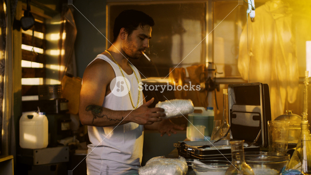 In the Underground Laboratory Smoking Dealer Places Brick Packs with Drugs Into Suitcase for Further Selling and Distribution. He Squats in the Abandoned Building with Boarded Up Windows.