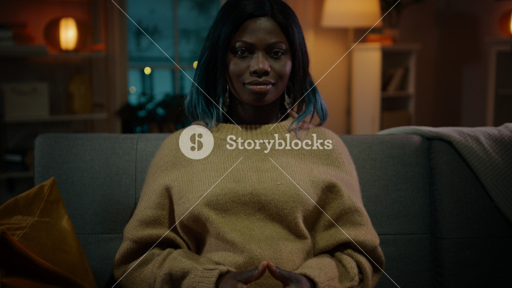 Portrait of a Beautiful Black Girl Sitting on a Couch at Home at Night, Watching Horror Movie on TV. She Gets Really Scared and Emotional.
