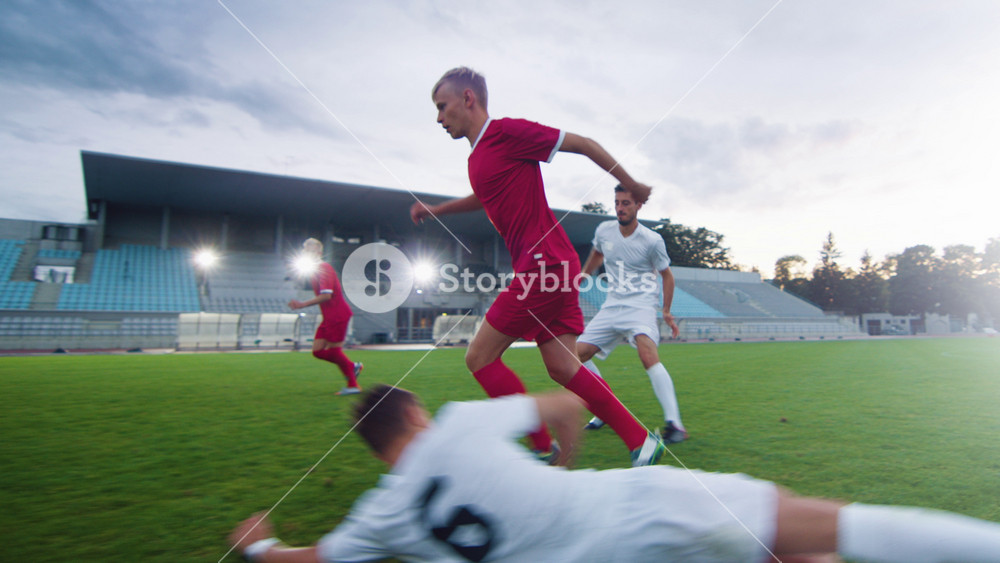 Professional Soccer Player Leads with a Ball, Masterfully Dribbling and Bypassing Sliding Tackles of His Opponents. Two Professional Football Teams Playing Important Match on a Field.