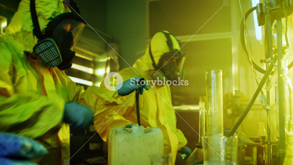 In the Underground Drug Laboratory Two Clandestine Chemists Wearing Protective Masks and Coveralls Use Hosepipe For Drug Distillation. They Cook Synthesised Drugs in the Abandoned Building.