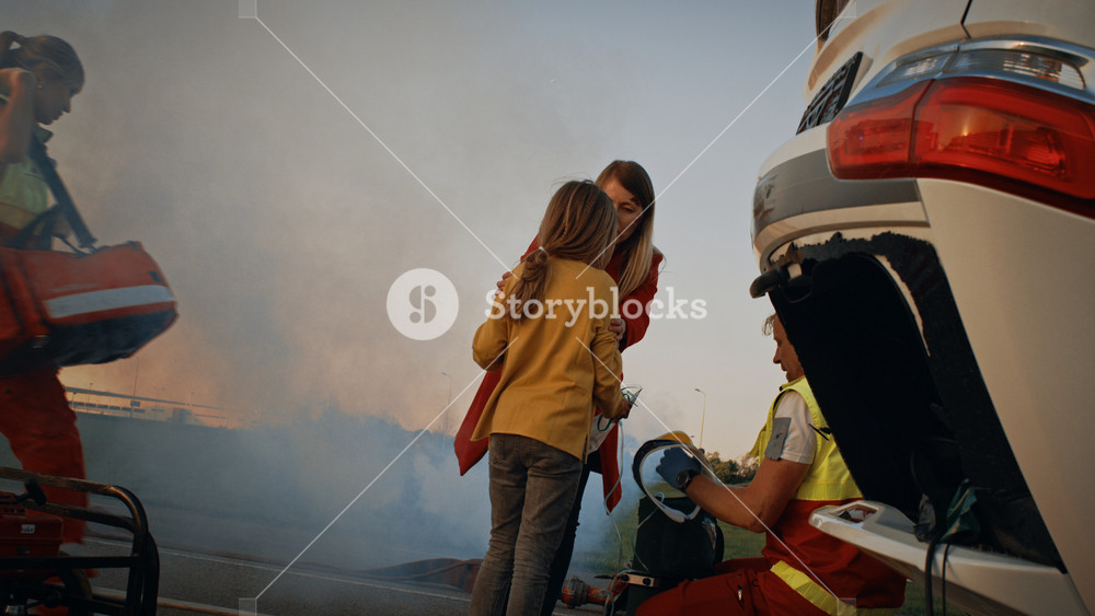 Car Crash Traffic Accident: Injured Young Girl Reunites with Her Loving Mother, Paramedic Gives Oxygen Mask. In the Background Rollover Car and Courageous Firemen Save Lives
