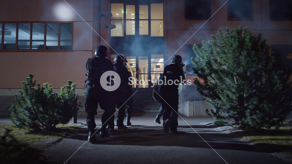 Masked Team of Armed SWAT Police Officers Run in Formation Forwards an Office Building. Soldiers with Rifles and Flashlights Run on a Street Filled with Smoke.