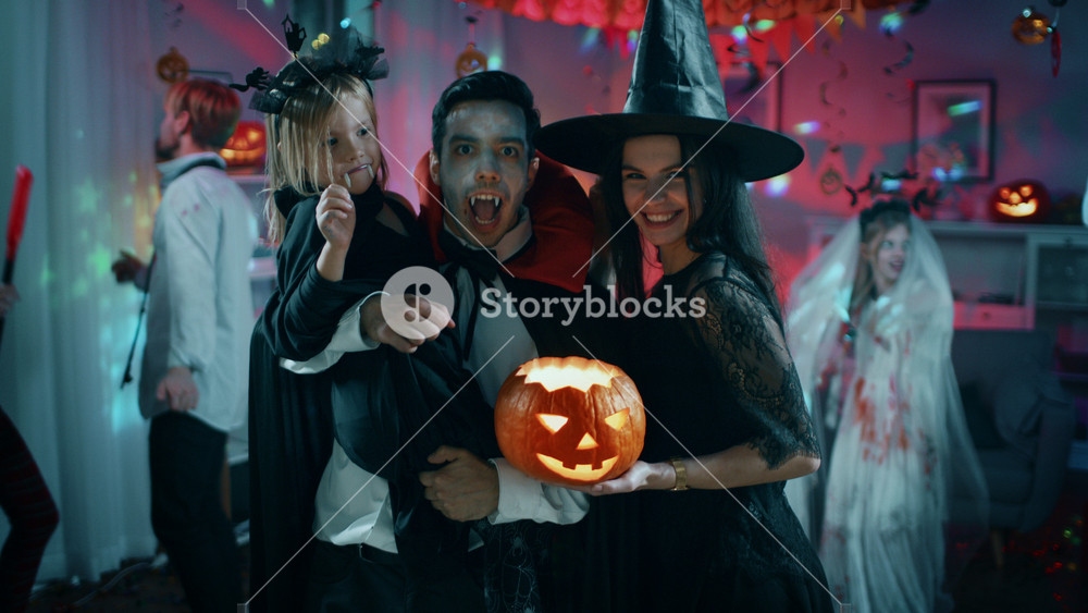 Halloween Costume Party: Father Count Dracula Holds Little Bat Girl Daughter and Hugs Witch Wife for a Happy Family Portrait. In the Background Monsters Having Fun