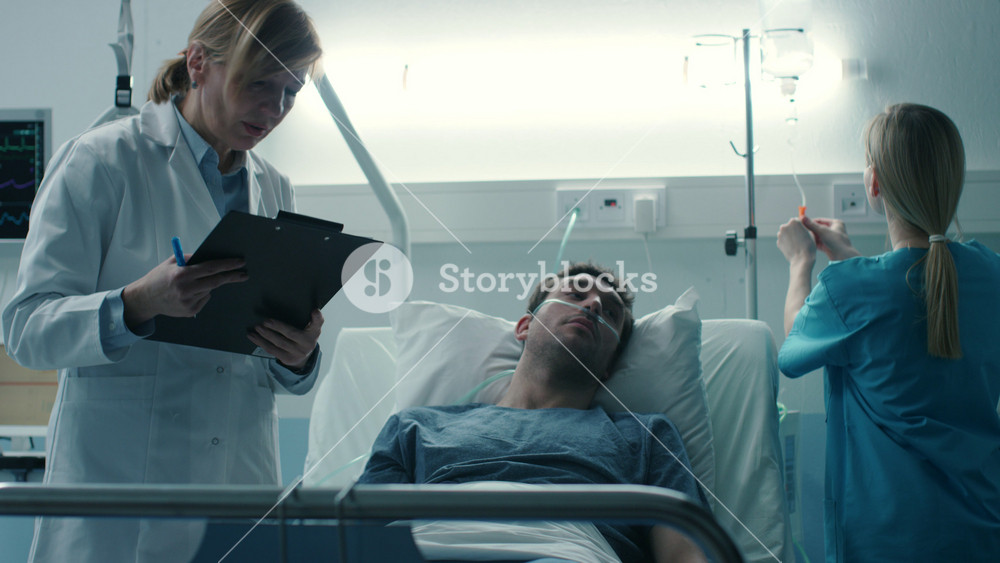 In the Hospital Sick Male Patient Lies on the Bed, Professional Female Doctor Writes in the Patient Chart, Addresses Nurse who Checks Drop Counter and Increases Dose of the Pain Killer.