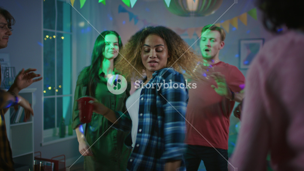 At the Wild House Party: Beautiful Black Girl Dances in Neon Lights, Holding Red Cup with Drink. In the Background Other Teenagers Having Fun, Clubbing.