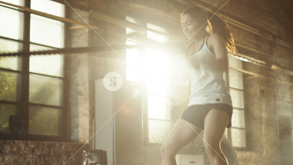 Athletic Woman in a Gym Exercises with Battle Ropes During Her Cross Fitness Workout High-Intensity Interval Training. She's Muscular and Sweaty, Gym is in Deserted Factory.