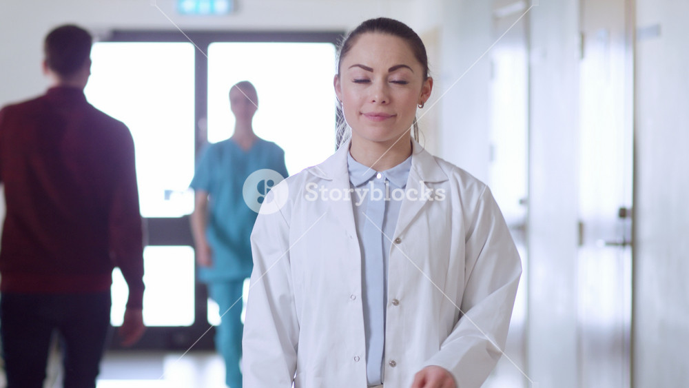 Focusing Shot of the Beautiful Young Female Doctor Walks Through the Hospital Hallway, She Stops, Crosses Arms and Charmingly Smiles. Professional People at Work.
