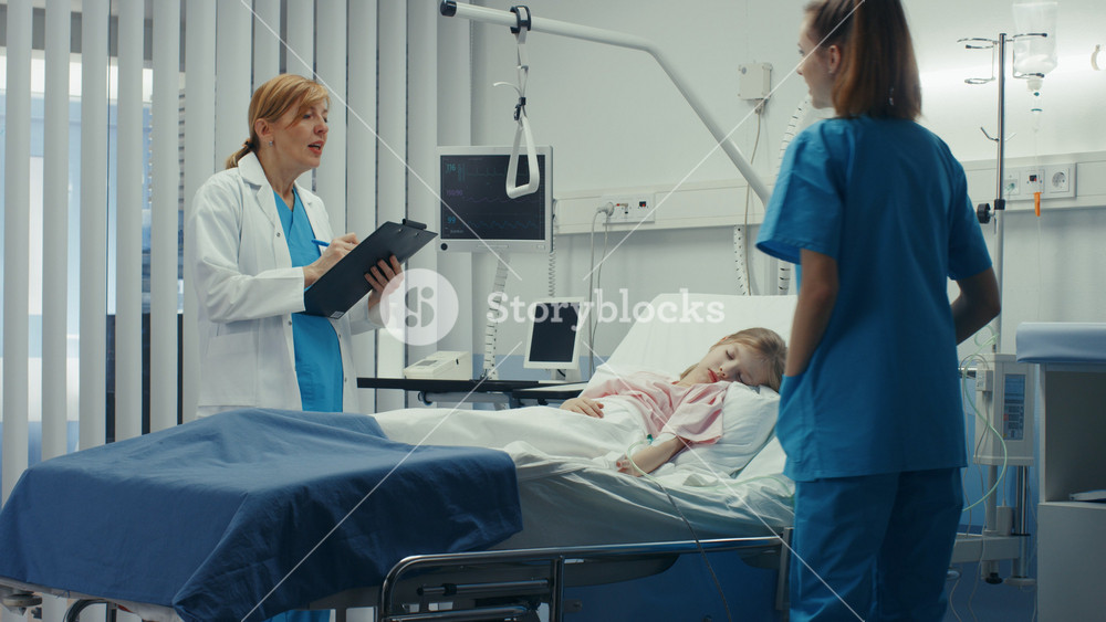 Sick Little Girl Lies on a Bed In the Hospital, Friendly Doctor Writes Medical Record/ Data into Clipboard, Talks with Nurse. Cute ill Child is Taken Care of in the Modern Pediatric/ Children Ward.