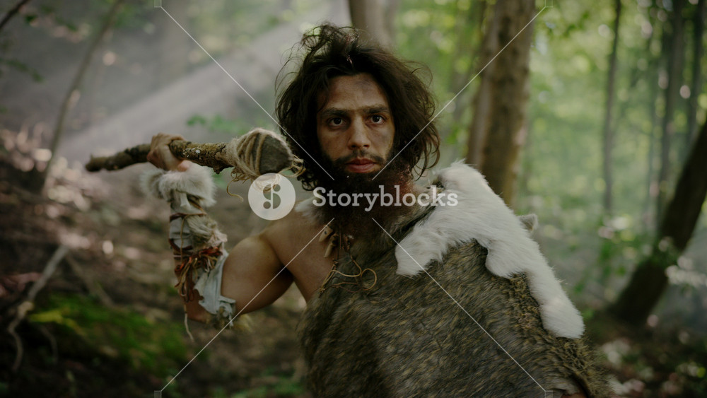 Portrait of Primeval Caveman Wearing Animal Skin and Fur Hunting with a Stone Tipped Spear in the Prehistoric Forest. Prehistoric Neanderthal Screaming, Threatening and Attacking