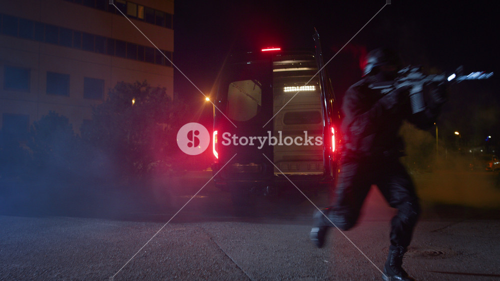 Masked Team of Armed SWAT Police Officers Exit a Black Van Parked Outside of an Office Building. Soldiers with Rifles and Flashlights Run on a Street Filled with Smoke.
