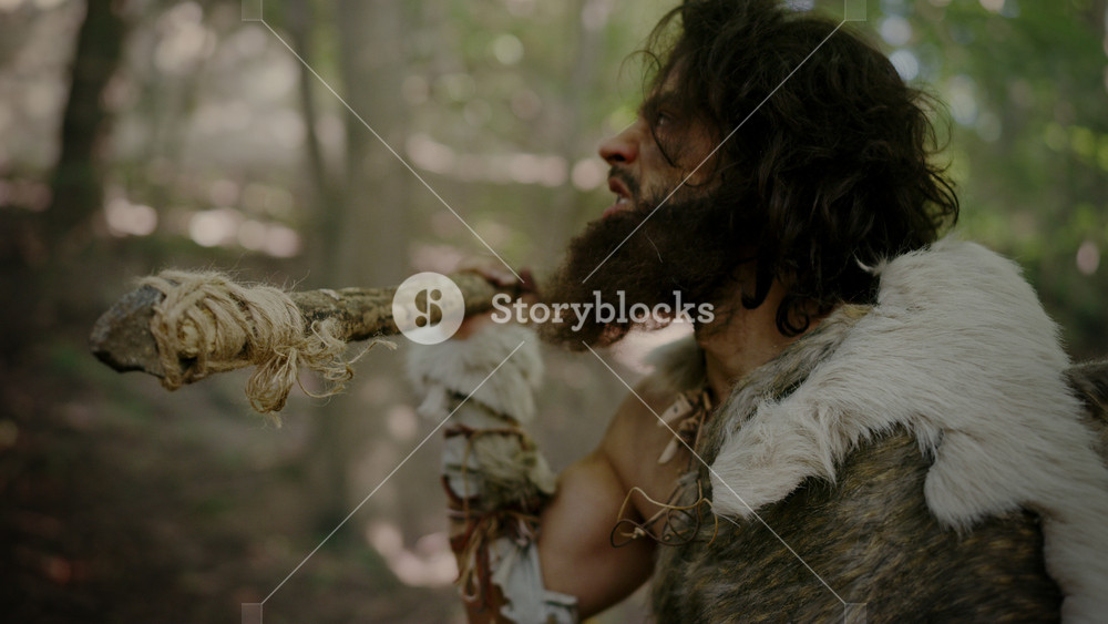 Portrait of Primeval Caveman Wearing Animal Skin and Fur Hunting with a Stone Tipped Spear in the Prehistoric Forest. Prehistoric Neanderthal Sneaking Ready to Throw Spear into Animal