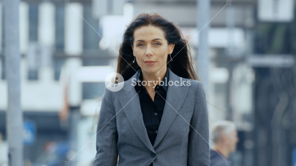 Medium Shot of the Business Woman in the Tailored Suit Walking on the Busy Big City Street in the Business District, Checks Her Smartphone. Confident Woman on Her Way to do Big Business.