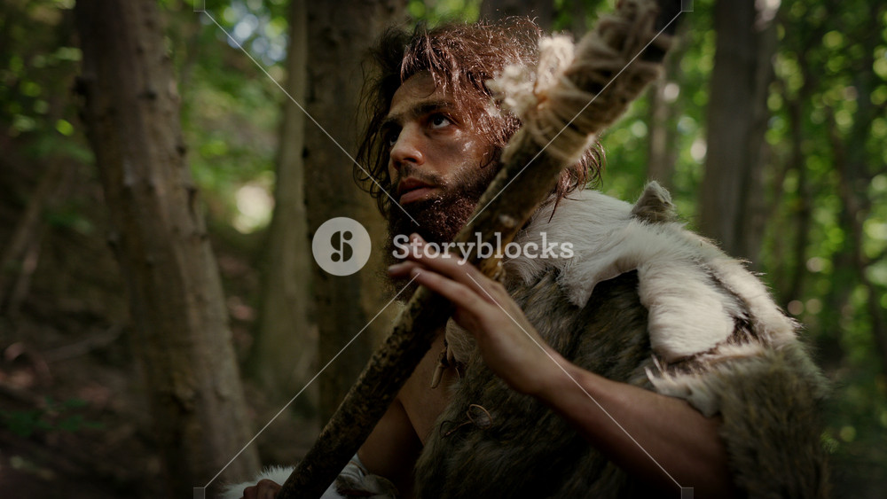 Portrait of Primeval Caveman Wearing Animal Skin and Fur Hunting with a Stone Tipped Spear in the Prehistoric Forest. Prehistoric Neanderthal Hunter Ready to Throw Spear in the Jungle