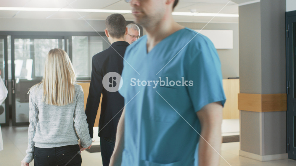 In the Hospital Following Shot of the Young Couple Holding Hands and Walking Towards Reception. Modern, Busy Hospital Facility.