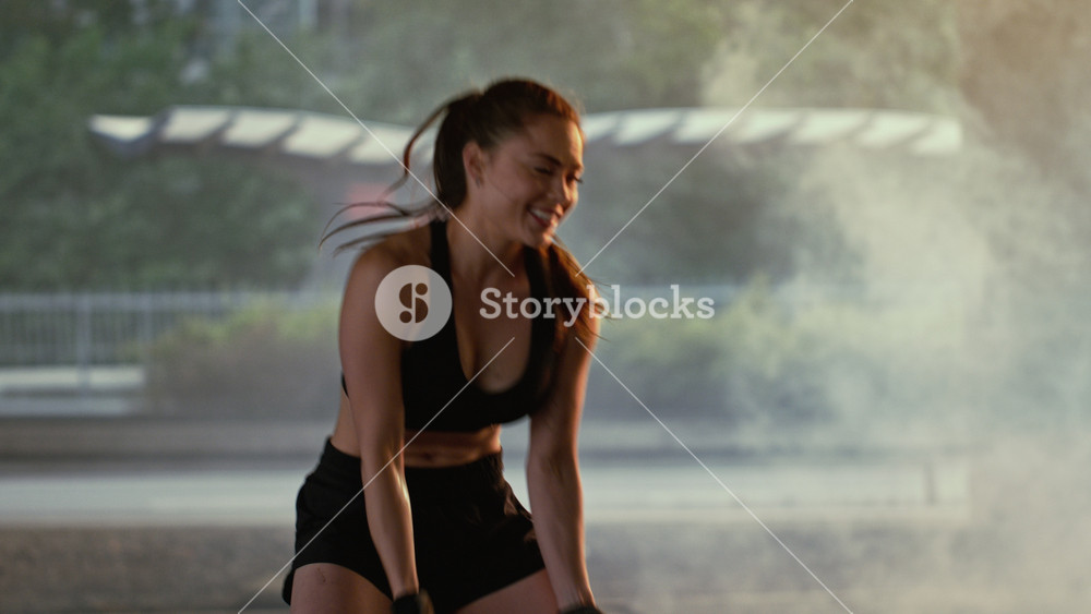 Beautiful Fitness Girl in Black Athletic Top and Shorts is Doing Exercises in the Street. She's Flipping a Big Heavy Tire.
