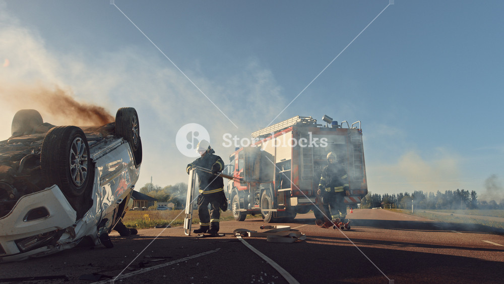Paramedics and Firefighters Arrive On the Car Crash Traffic Accident Scene. Professionals Rescue Injured Victim Trapped in Rollover Vehicle by Extricating Them, giving First Aid and Extinguishing Fire