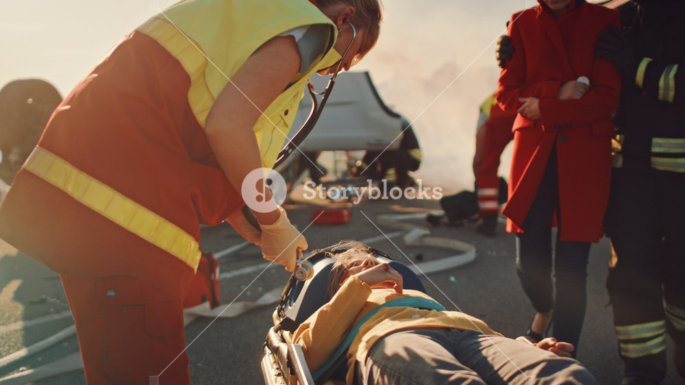 On the Car Crash Traffic Accident Scene: Paramedics Saving Life of a Little Girl Lying on Stretchers, Shes given First Aid Help. Firefighter Leads Mother To Daughter. In Background Rollover Vehicle