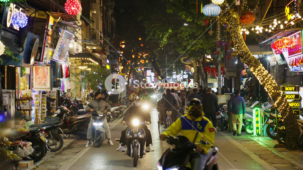 Nighttime traffic and bustling street life with pedestrians and mopeds in vibrant Old Quarter of Hanoi, Vietnam, showcasing city's lively