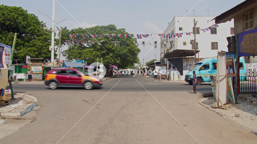 Street scene with busy traffic and pedestrians crossing an intersection in developing neighbourhood of Accra, capital city of Ghana, West