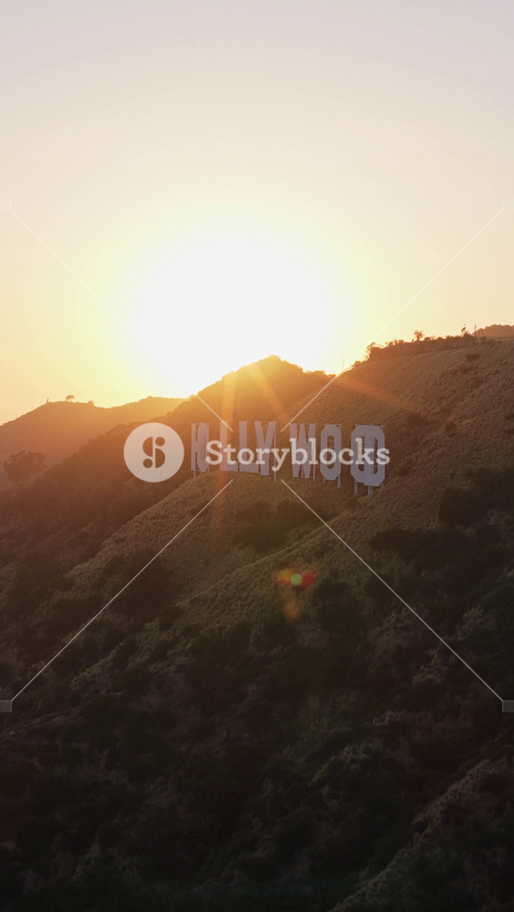 Golden sun over Hollywood Sign and communication tower in Los Angeles, California, with distant city skyline peeking through morning haze