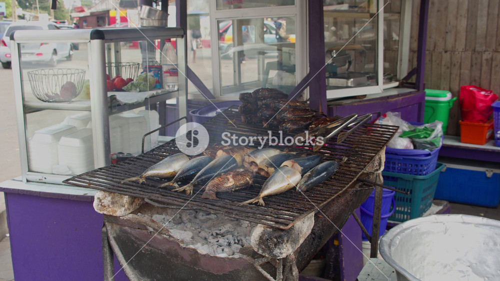Fresh fish sizzling on charcoal barbecue at bustling street food market stall in Accra, Ghana, popular west african culinary tradition and