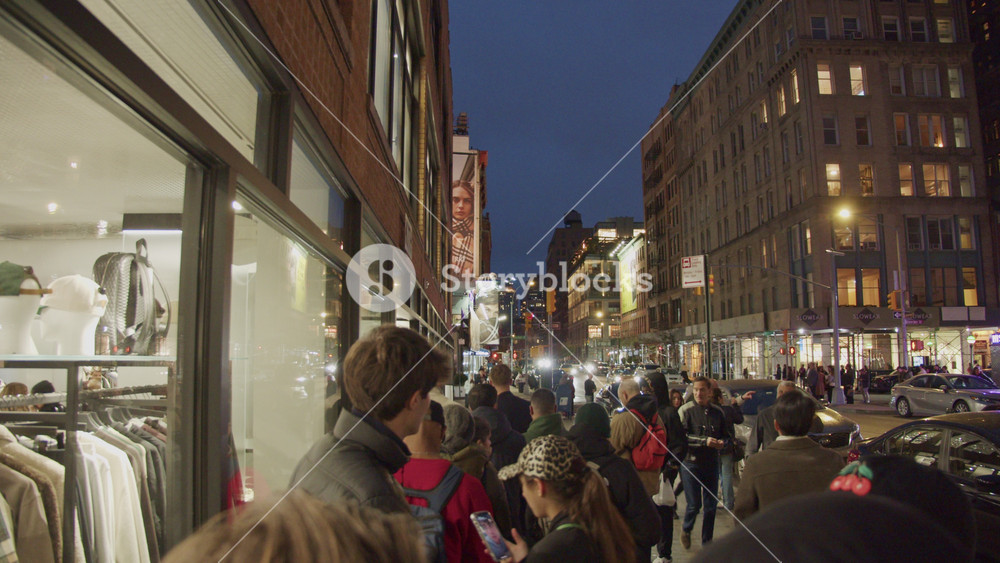 Urban landscape capturing pedestrians moving and queuing along New York sidewalk near clothing store during dusk in Manhattan. NYC, USA, 11