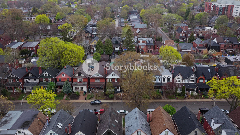 Residential neighborhood with typical victorian style houses, lush green trees and streets with cars during quiet day in North America