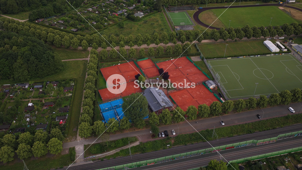 Top down aerial of a tennis club with red clay courts and blue hard courts next to a football pitch and running track in suburban Frankfurt