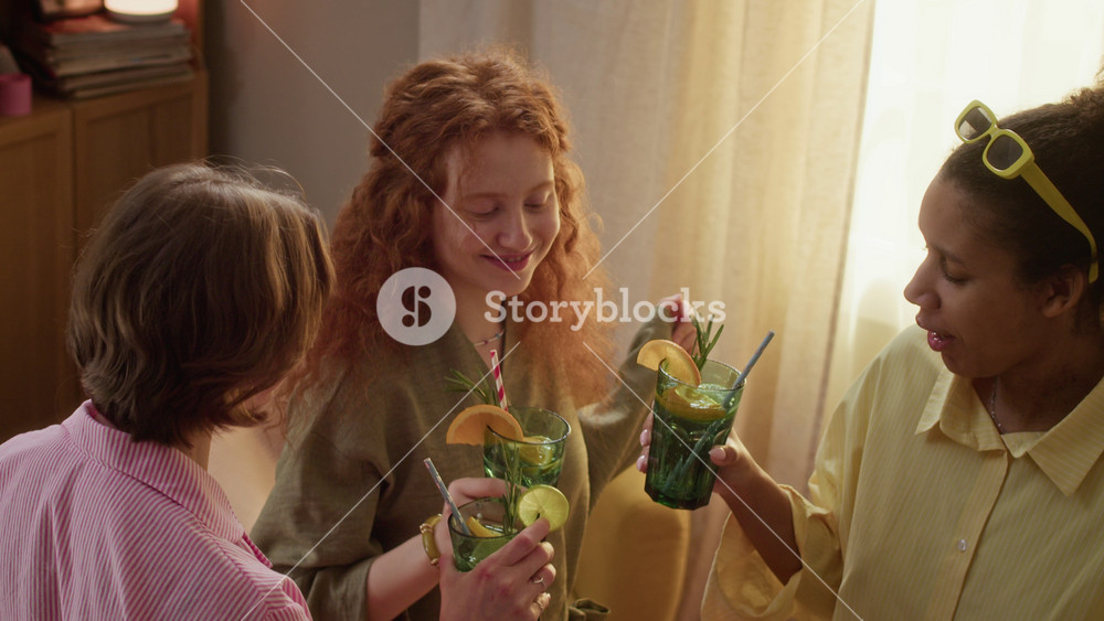 Diverse young adult women, including Caucasian and African American friends, clinking glasses with cocktails and laughing at friendly gathering. Ideal for beverage ads or lifestyle campaigns