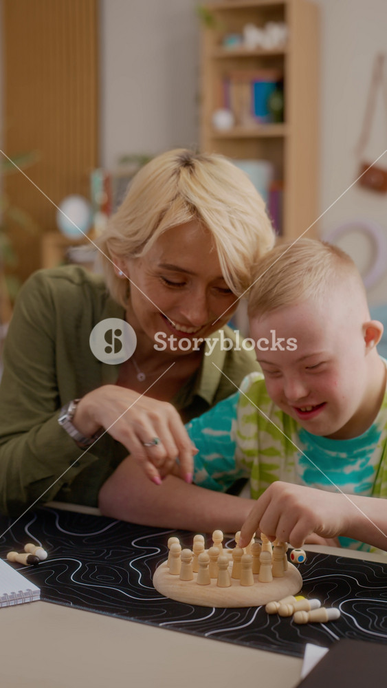Vertical video of Caucasian female therapist helping boy with Down syndrome playing wooden board game. Clip perfect for promoting special education, cognitive therapy, and social inclusion