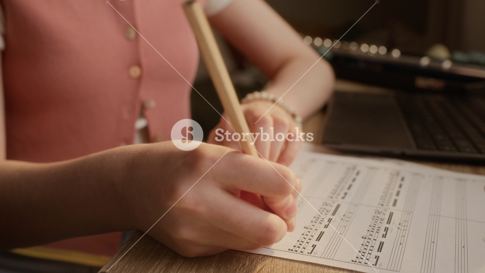 Tilt up shot of Caucasian child writing notes on sheet music with pencil during home music lesson. Clip is perfect for promoting youth music education, online tutoring, and creative learning programs