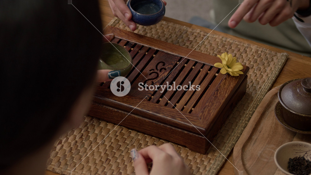 Handheld shot of two people emptying cups from tea and pouring it onto wooden tray as part of tea ceremony ritual at home