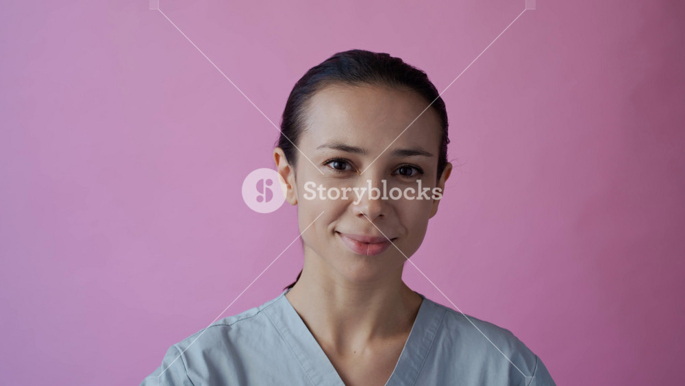 Zoom in copy space portrait of female Caucasian young doctor in medical uniform placing pink ribbon on chest as symbol of breast cancer awareness