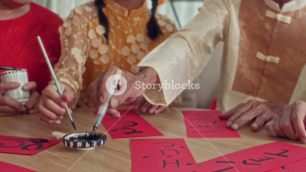 Tilt down shot of teenage granddaughter with grandparents writing calligraphy on red paper while celebrating Tet at home
