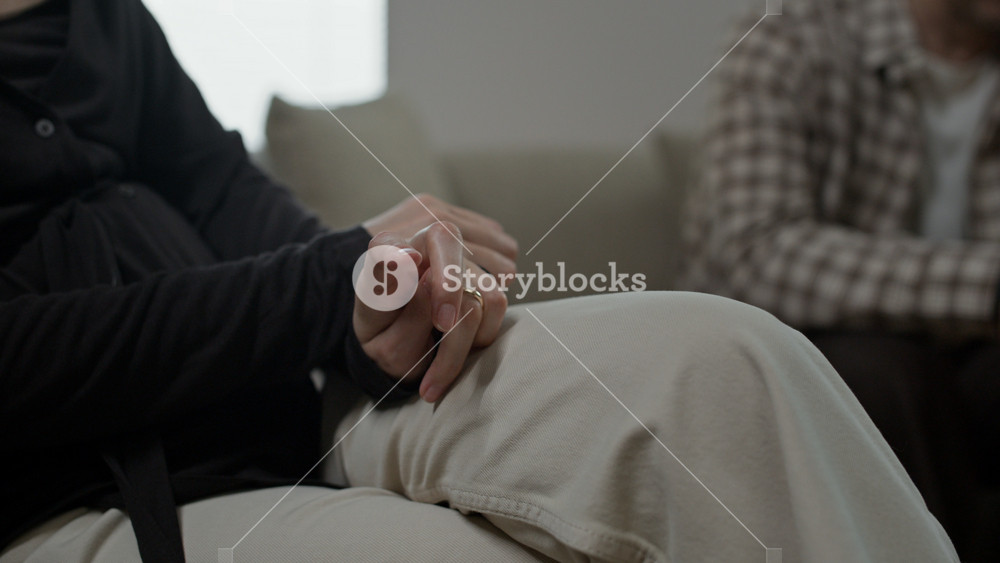 Close up of woman holding napkin and touching golden wedding ring while her spouse sitting near her during family therapy in office