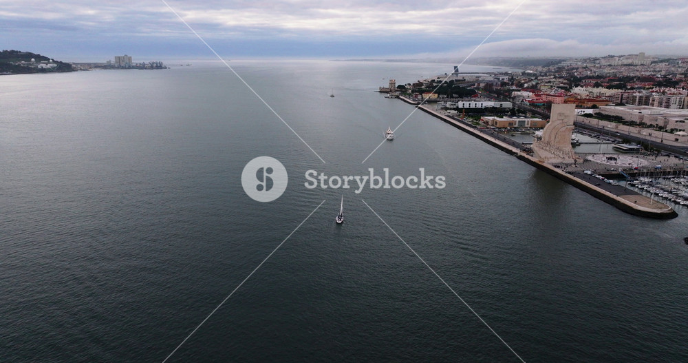 Aerial approach along the Tagus River revealing Lisbon harbor and urban edge under calm light, clean cinematic European travel establishing shot