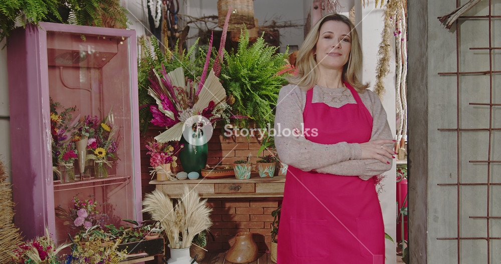 Flower shop owner stands among colorful floral arrangements, expressing entrepreneurial confidence, retail success and authentic local business leadership in a welcoming boutique