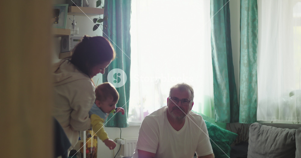 Mother holding baby while father watches from couch in cozy living room, joyful family bonding moment with infant, nurturing and warm atmosphere at home
