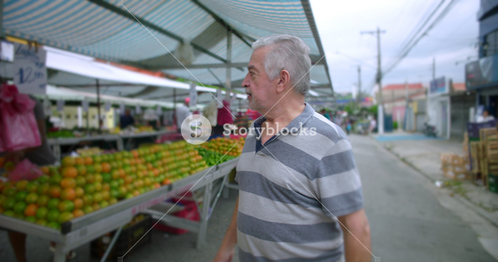 Elderly man greeting street vendor while walking through local food market expressing neighborliness familiarity and everyday social bonds within community street commerce