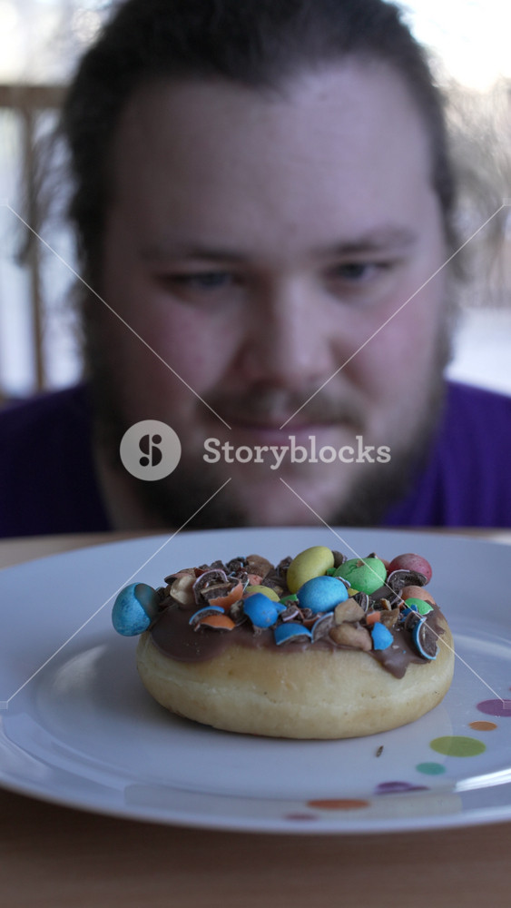 Overweight Person wanting to eat sugar food on plate. One Young fat man in diet fasting from junk food. Donut closeup in front of fat guy in Vertical Video