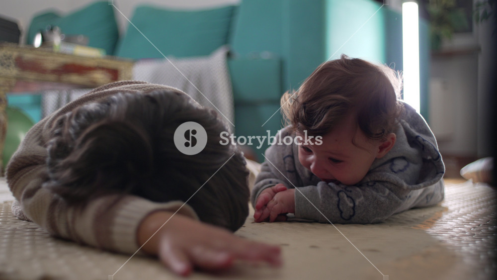 Baby crying on floor beside older brother, expressing distress and discomfort in intimate family home scene showing emotion, vulnerability, and sibling presence