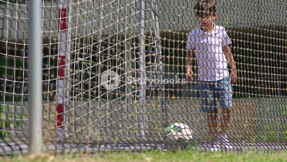 Soccer ball rolling inside goal net after kick on outdoor sports field, childhood football practice moment capturing movement achievement and playful athletic activity