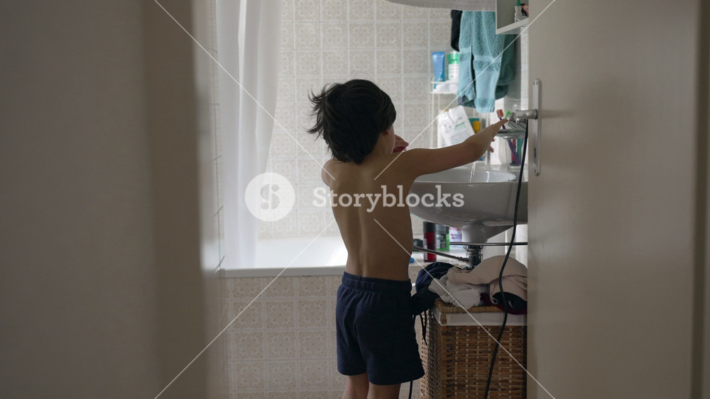 Boy standing at bathroom sink, washing hands, home interior, daily hygiene routine, child’s morning activities, view through doorway, home life, personal care, domestic scene