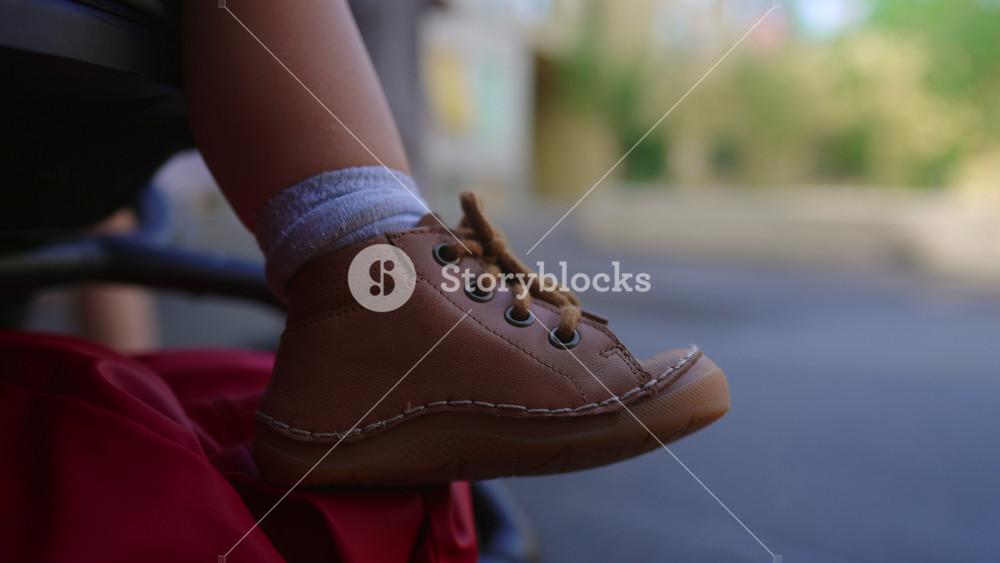 Toddler feet wearing small shoes resting on stroller footrest during outdoor walk expressing calm routine movement and everyday family life in urban environment
