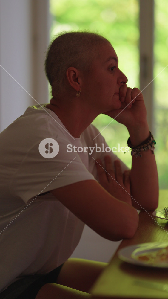 Woman with cancer reflecting quietly at dining table, contemplating life, resilience, hope and emotional strength during everyday family moments