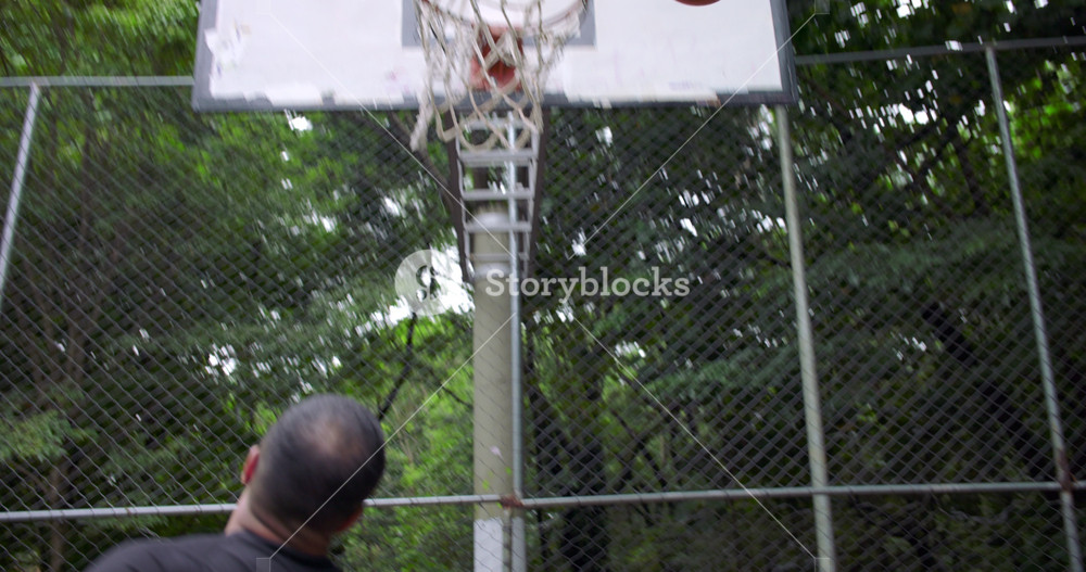 Hispanic man jumps to score in basketball net but misses, teammate catches rebound and passes the ball to continue fast-paced street game, handheld action on outdoor court