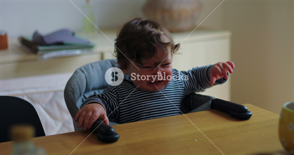 Anxious baby boy reaches for mother's hand from high chair during mealtime at home, finding comfort, emotional security and calm through parental reassurance and connection