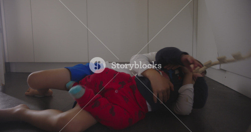 Two young brothers lying on the kitchen floor laughing and playing together, expressing sibling affection, carefree childhood, and the joyful intimacy of family life at home
